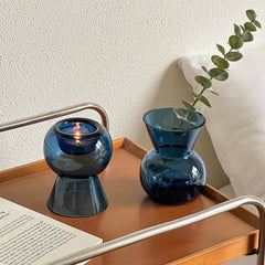 Blue glass candle holder and matching glass vase side by side on a wooden tray.