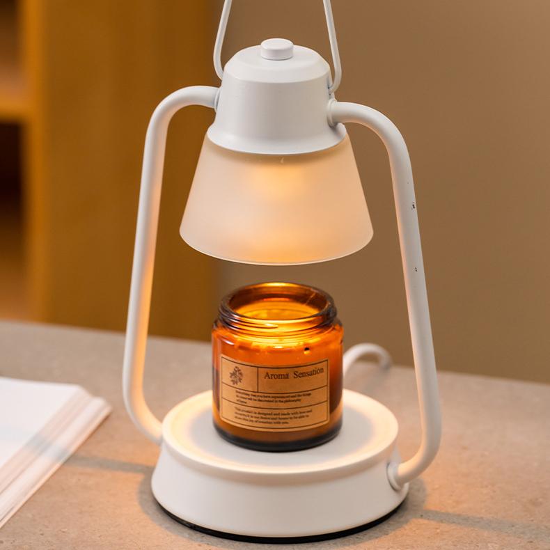 Minimalist white candle warmer lamp illuminating an amber glass scented candle on a cozy desk