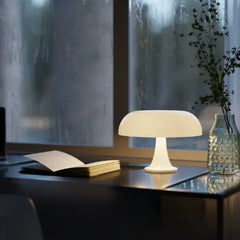 The Serene Glow Mushroom Desk Lamp casts a warm, inviting light on a book, creating a tranquil reading sanctuary on a desk during a quiet evening.