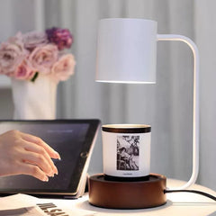 Minimalist candle warmer lamp with solid wood base lighting up a candle on a work desk with flowers and tablet