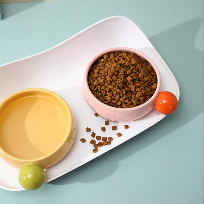 Pink and yellow Sugar Bean Ceramic Cat Bowls with bits of kibble on tray, anti-spill feature