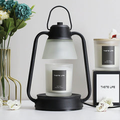 Vintage-style black candle warmer lamp with frosted glass shade and scented candle on a minimal table setting