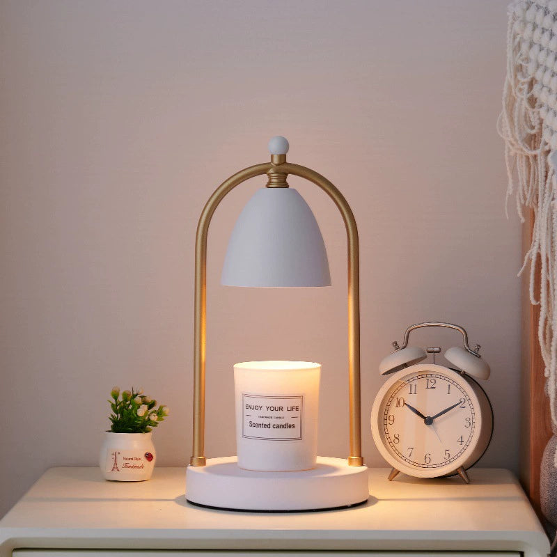 White and gold candle warmer lamp showcasing soft lighting with a white scented candle on a nightstand, creating a serene mood.